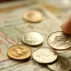 Крупный план руки, держащей монеты, на фоне графиков и диаграмм, символизирующих финансовый анализ
